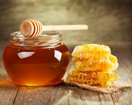 jar of honey with honeycomb on wooden table